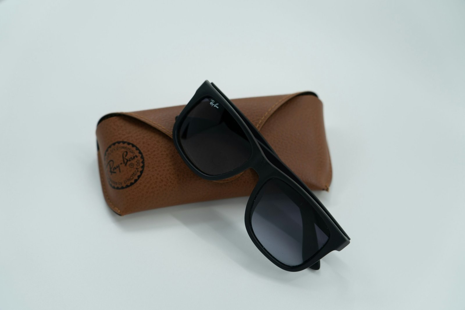 Black sunglasses with dark lenses placed on a brown leather Ray-Ban case, set against a plain light background.